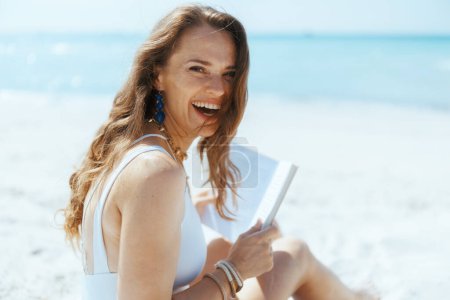 Photo for Smiling stylish woman on the beach with straw bag and book. - Royalty Free Image