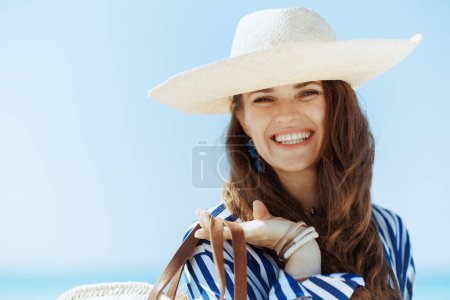 Foto de Retrato de mujer de mediana edad con estilo sonriente en la orilla del océano con sombrero de paja. - Imagen libre de derechos