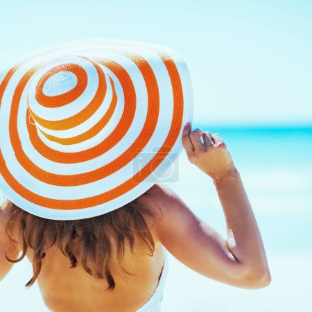 Téléchargez les photos : Jeune femme en maillot de bain chapeau de plage regardant au loin. vue arrière - en image libre de droit