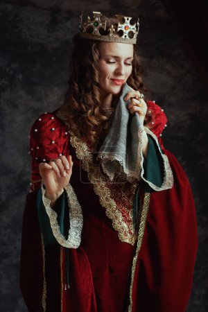 Foto de Reina medieval sonriente en vestido rojo con pañuelo y corona sobre fondo gris oscuro. - Imagen libre de derechos