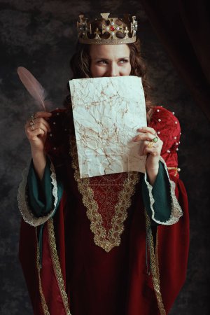 Foto de Reina medieval en vestido rojo con pergamino y corona sobre fondo gris oscuro. - Imagen libre de derechos