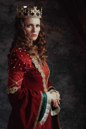 Téléchargez les photos : Reine médiévale en robe rouge avec couronne sur fond gris foncé. - en image libre de droit