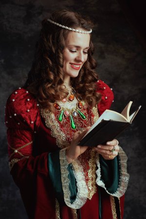Photo for Smiling medieval queen in red dress with book on dark gray background. - Royalty Free Image