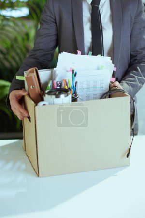 Photo for New job. Closeup on modern female worker in modern green office in grey business suit with personal belongings in cardboard box. - Royalty Free Image