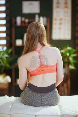 Photo for Healthcare time. Seen from behind teenage girl in medical massage therapist cabinet with crooked back sitting on massage table. - Royalty Free Image