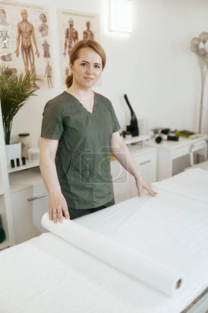 Photo for Healthcare time. concerned massage therapist woman in massage cabinet with disposable sheet preparing for new client. - Royalty Free Image