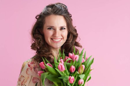 Téléchargez les photos : Portrait de femme moderne heureuse avec de longs cheveux bruns ondulés avec bouquet de tulipes isolées sur rose. - en image libre de droit