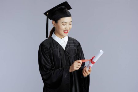 Photo for Happy young female asian graduate student with diploma isolated on gray background. - Royalty Free Image