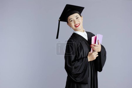 Foto de Feliz joven mujer asiática graduado estudiante con libros y cuadernos sobre gris fondo. - Imagen libre de derechos