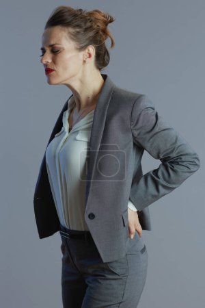 Photo for Tired elegant middle aged woman employee in grey suit having back pain isolated on gray background. - Royalty Free Image