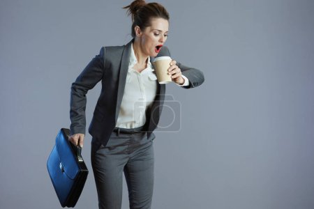 Téléchargez les photos : Femme élégante choquée travailleur en costume gris avec tasse de café et mallette courir isolé sur fond gris. - en image libre de droit