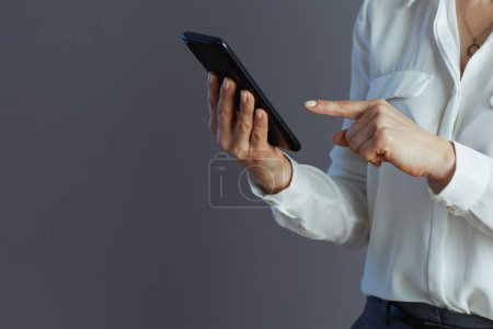 Foto de Primer plano de la mujer de mediana edad empleada en blusa blanca que se comunica en las redes sociales utilizando un teléfono inteligente aislado en un fondo gris. - Imagen libre de derechos