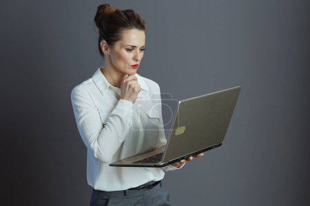Téléchargez les photos : Cher élégant 40 ans femme travailleur en chemisier blanc avec ordinateur portable isolé sur gris. - en image libre de droit