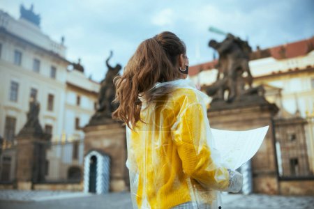Foto de Visto desde atrás viajero solo mujer en blusa amarilla y impermeable en Praga República Checa con mapa cerca del Castillo de Praga. - Imagen libre de derechos