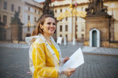 Téléchargez les photos : Heureuse jeune femme en chemisier jaune et imperméable à Prague République tchèque avec carte près de Château de Prague. - en image libre de droit