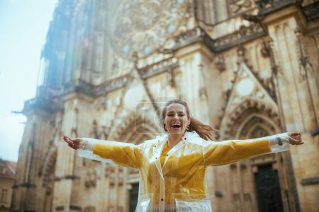Photo for Happy trendy solo traveller woman in yellow blouse and raincoat in Prague Czech Republic enjoying promenade and rejoicing. - Royalty Free Image