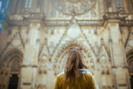 Photo for Seen from behind woman in yellow blouse and raincoat in Prague Czech Republic exploring attractions. - Royalty Free Image