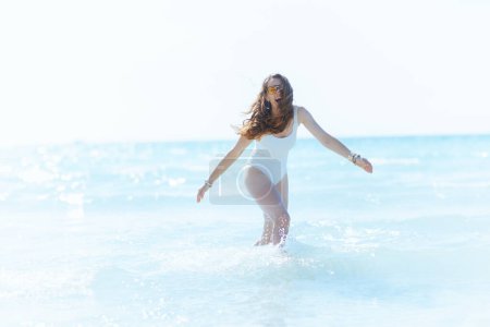 Téléchargez les photos : Souriant moderne femelle sur la plage avoir du plaisir dans l'eau. - en image libre de droit