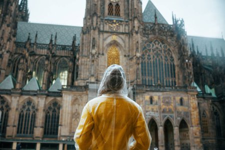 Photo for Seen from behind solo traveller woman in yellow blouse and raincoat in Prague Czech Republic sightseeing. - Royalty Free Image