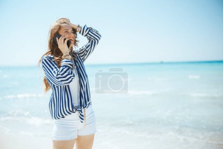 Téléchargez les photos : Heureuse femme d'âge moyen élégante sur le bord de la mer parlant sur un smartphone. - en image libre de droit