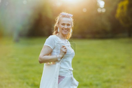 Foto de Hora de verano. mujer de moda feliz en camisa blanca con bolso de mano en el prado al aire libre. - Imagen libre de derechos
