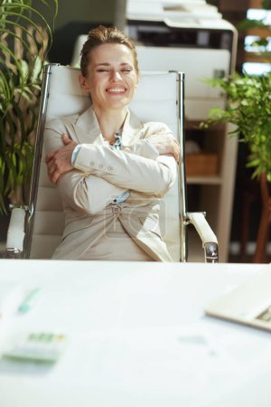 Foto de Feliz moderna 40 años de edad contable mujer en un traje de negocios ligero en la oficina verde moderna abrazándose. - Imagen libre de derechos