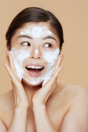 Téléchargez les photos : Moderne asiatique femme lavage visage sur beige fond. - en image libre de droit
