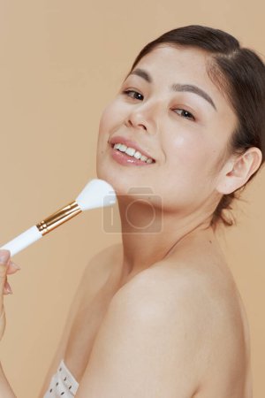 Téléchargez les photos : Moderne asiatique femelle avec maquillage brosse sur fond beige. - en image libre de droit