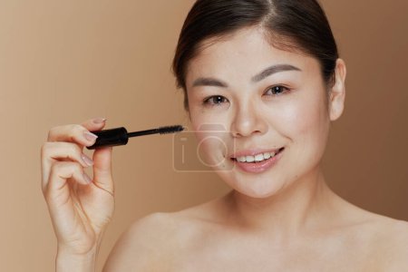 Photo for Portrait of young woman with mascara against beige background. - Royalty Free Image