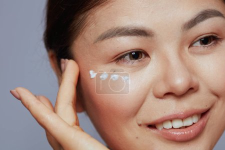 Téléchargez les photos : Moderne asiatique femelle avec crème pour les yeux sur le visage sur fond bleu. - en image libre de droit