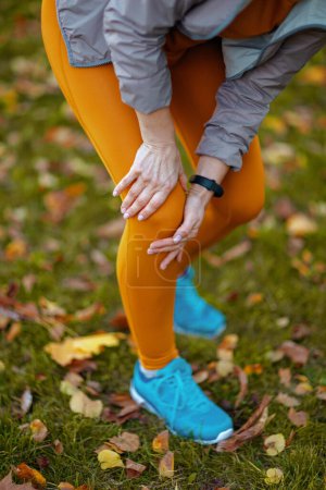 Foto de Hola otoño. Primer plano de la mujer en ropa de fitness en el parque con dolor de rodilla. - Imagen libre de derechos