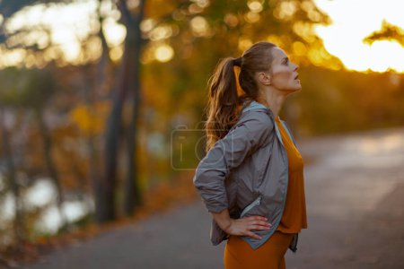 Foto de Hola otoño. ajuste relajado mujer de 40 años en ropa de fitness en el parque relajante después del entrenamiento. - Imagen libre de derechos
