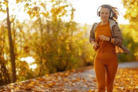 Téléchargez les photos : Bonjour l'automne. femme à la mode en vêtements de fitness dans le parc à l'écoute de la musique avec écouteurs et courir. - en image libre de droit