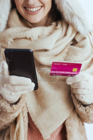Téléchargez les photos : Gros plan sur femme souriante isolée sur fond blanc en gants blancs avec carte de crédit et smartphone. - en image libre de droit