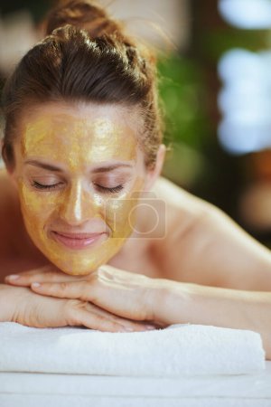 Photo for Healthcare time. relaxed modern woman in spa salon with golden cosmetic mask on face laying on massage table. - Royalty Free Image