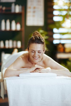 Téléchargez les photos : Temps de santé. femme moderne heureuse dans le salon de spa pose sur la table de massage. - en image libre de droit
