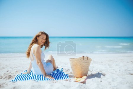 Téléchargez les photos : Heureux élégant femelle sur la plage avec sac de paille et serviette rayée. - en image libre de droit