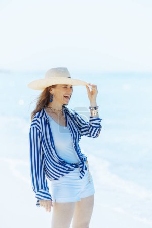 Foto de Sonriente mujer moderna en la orilla del mar con sombrero de paja. - Imagen libre de derechos