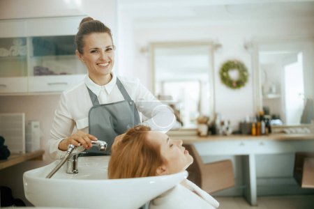 Friseurin mittleren Alters in modernem Haarstudio mit Client, der Haare wäscht.