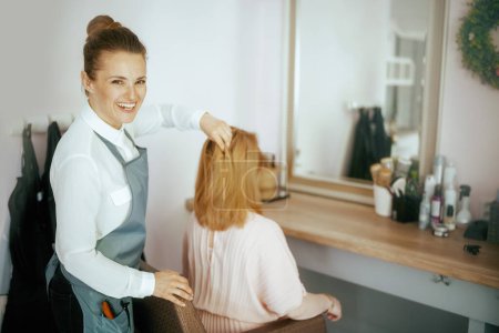 Téléchargez les photos : Femme d'âge moyen coiffeur dans un studio de coiffure moderne avec client. - en image libre de droit