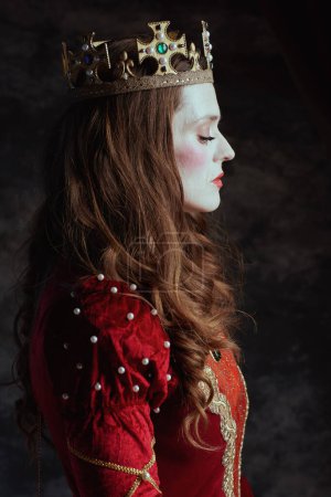 Foto de Reina medieval en vestido rojo con maquillaje blanco y corona sobre fondo gris oscuro. - Imagen libre de derechos