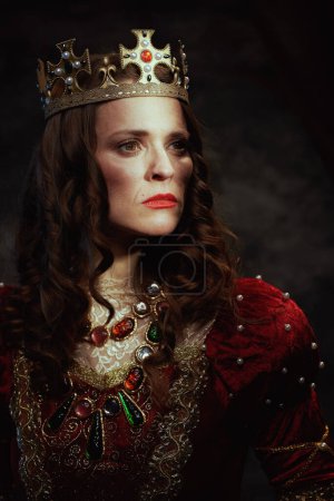Téléchargez les photos : Reine médiévale en robe rouge avec couronne sur fond gris foncé. - en image libre de droit