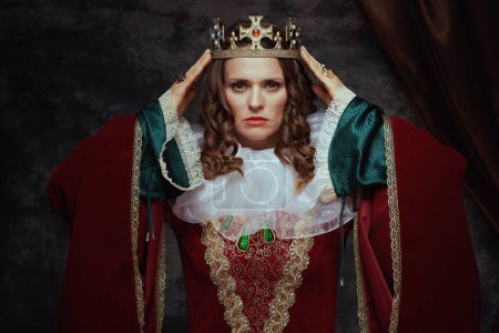 Photo for Medieval queen in red dress with white collar and crown on dark gray background. - Royalty Free Image