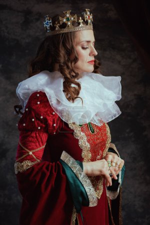 Téléchargez les photos : Reine médiévale en robe rouge avec col blanc et couronne sur fond gris foncé. - en image libre de droit