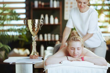 Photo for Healthcare time. female medical massage therapist in massage cabinet with clipboard, teenage client and award cup making massage. - Royalty Free Image