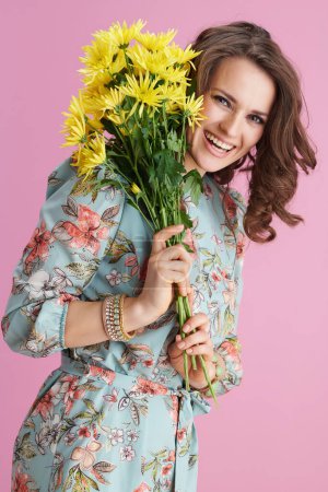 Photo for Happy stylish woman with long wavy brunette hair with yellow chrysanthemums flowers against pink background. - Royalty Free Image