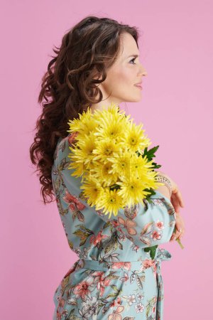 Téléchargez les photos : Chère femelle moderne avec de longs cheveux bruns ondulés avec des fleurs de chrysanthèmes jaunes sur fond rose. - en image libre de droit