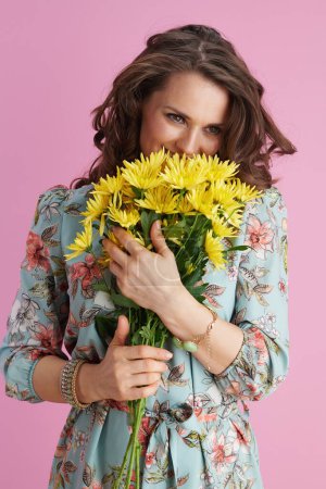 Photo for Smiling trendy woman in floral dress with yellow chrysanthemums flowers isolated on pink background. - Royalty Free Image