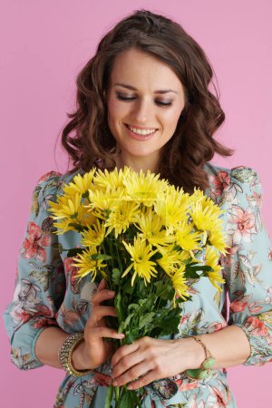 Photo for Happy modern woman with long wavy brunette hair with yellow chrysanthemums flowers isolated on pink. - Royalty Free Image