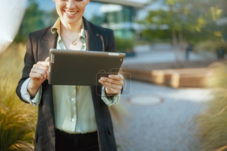 Foto de Primer plano de la mujer trabajadora sonriente cerca del centro de negocios en chaqueta negra con tablet PC. - Imagen libre de derechos